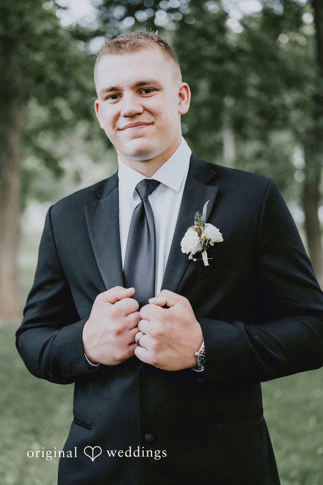Emily + Ethan Groom in a black suit smiling for a portrait.