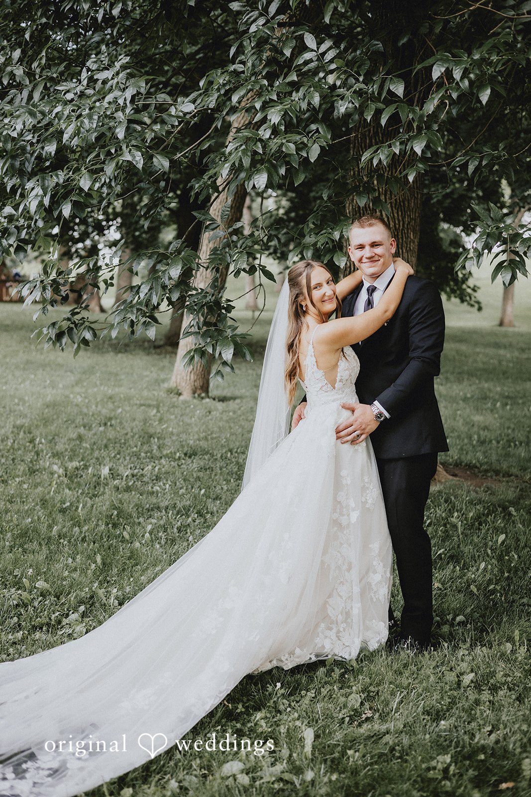 Emily + Ethan Groom lifting the bride in an embrace on a grassy field.