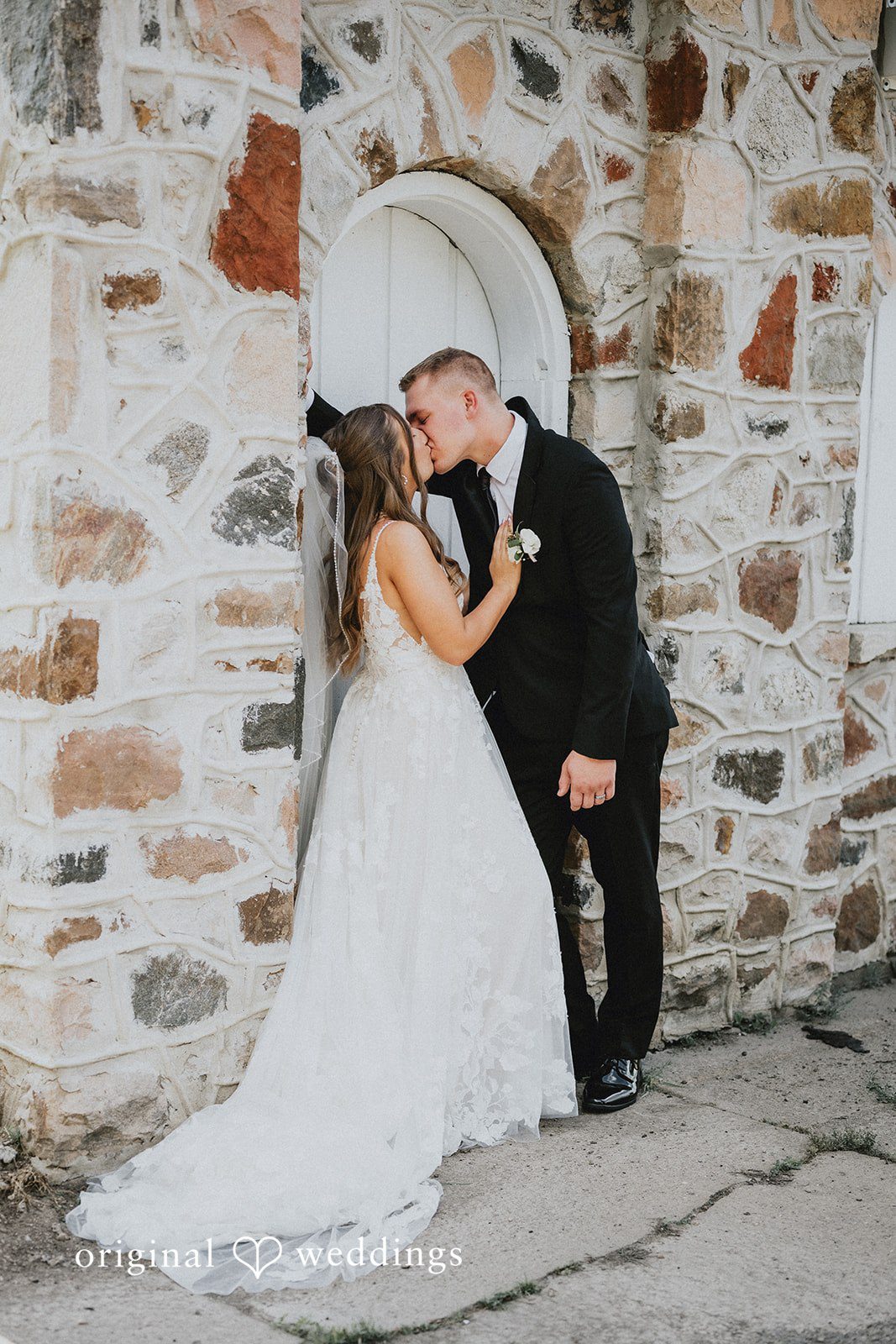 Emily + Ethan Bride and groom kissing against a rustic stone wall.