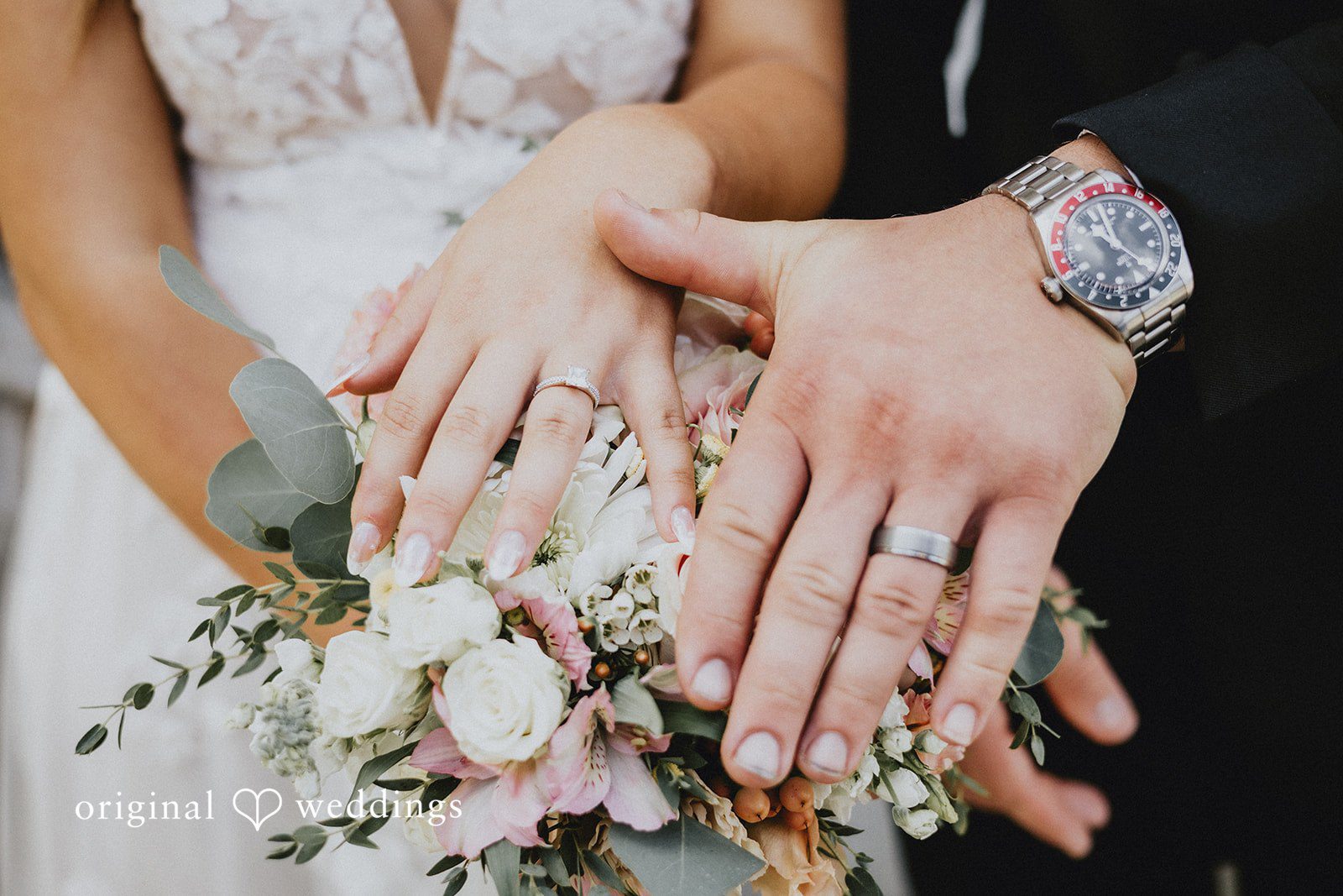 Emily + Ethan Close-up view of the bride and groom showing off their wedding rings over a bouquet.