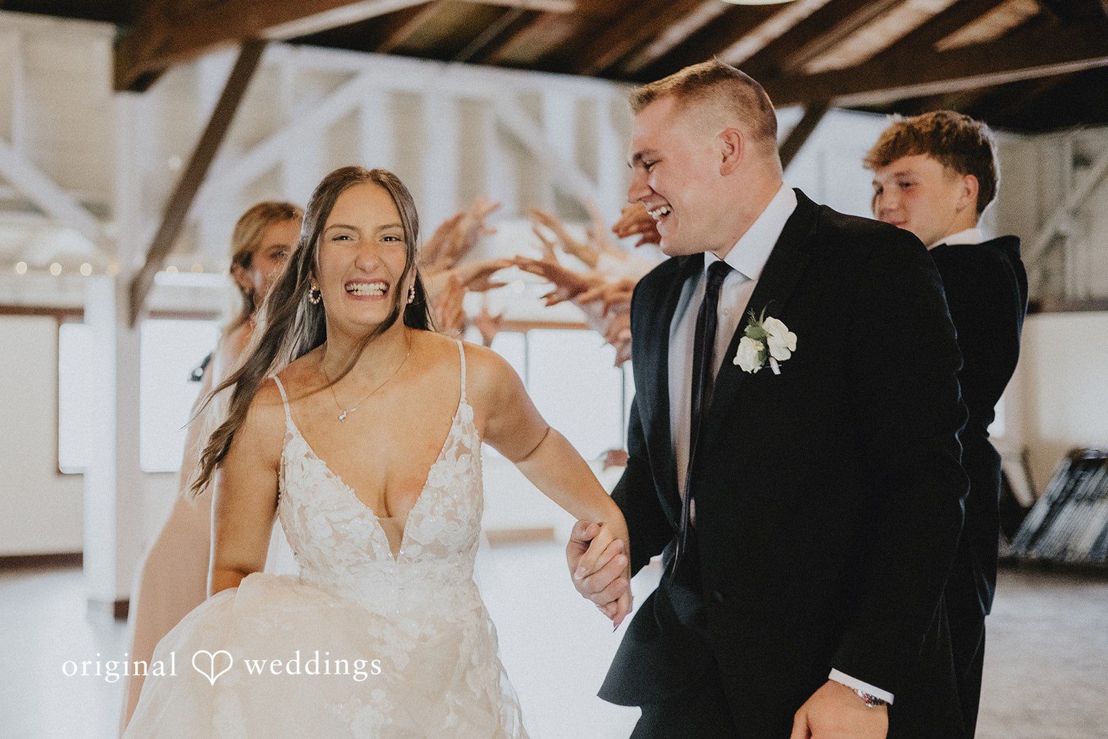 Emily + Ethan Newlyweds walking hand-in-hand through a crowded reception area.