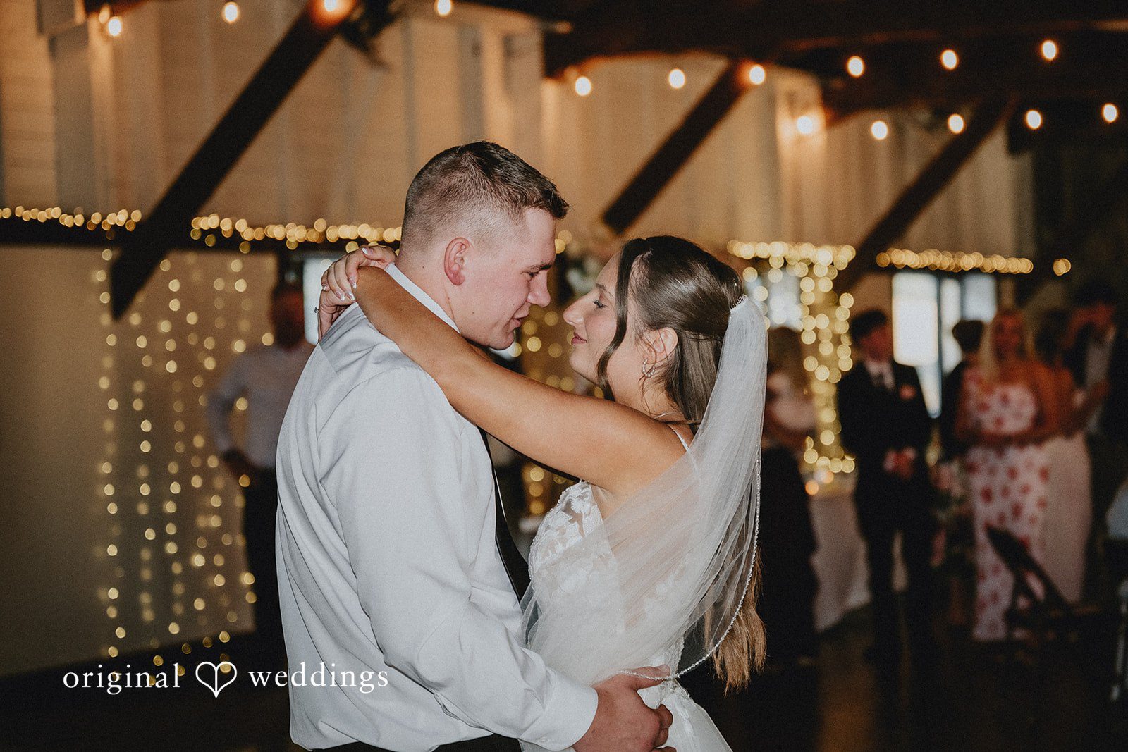 Emily + Ethan Newlyweds dancing closely together under string lights at the reception.