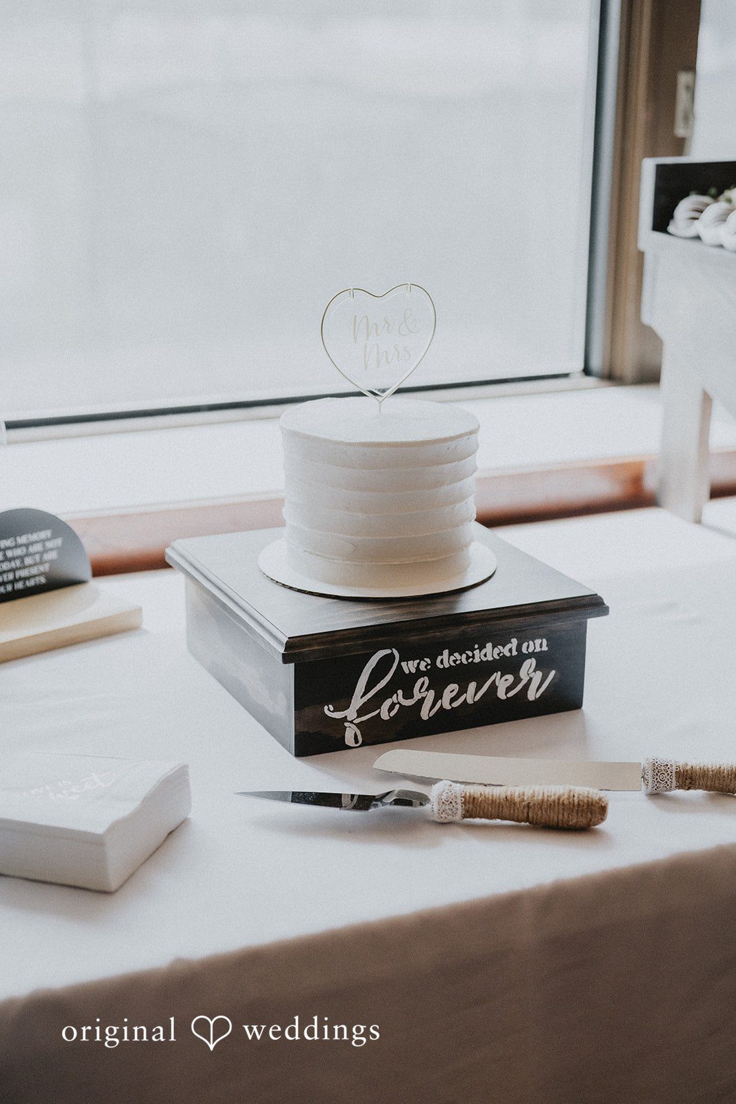 Emily + Ethan A small white wedding cake on a dark wooden stand featuring the inscription "we decided on forever."