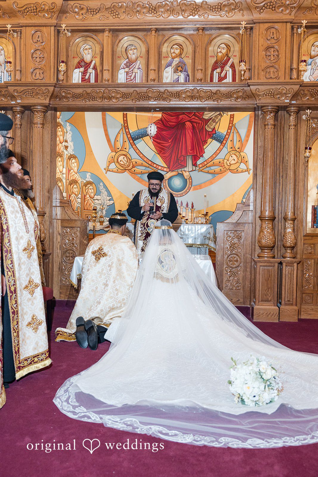 A bride and groom kneeling before a priest at the altar.