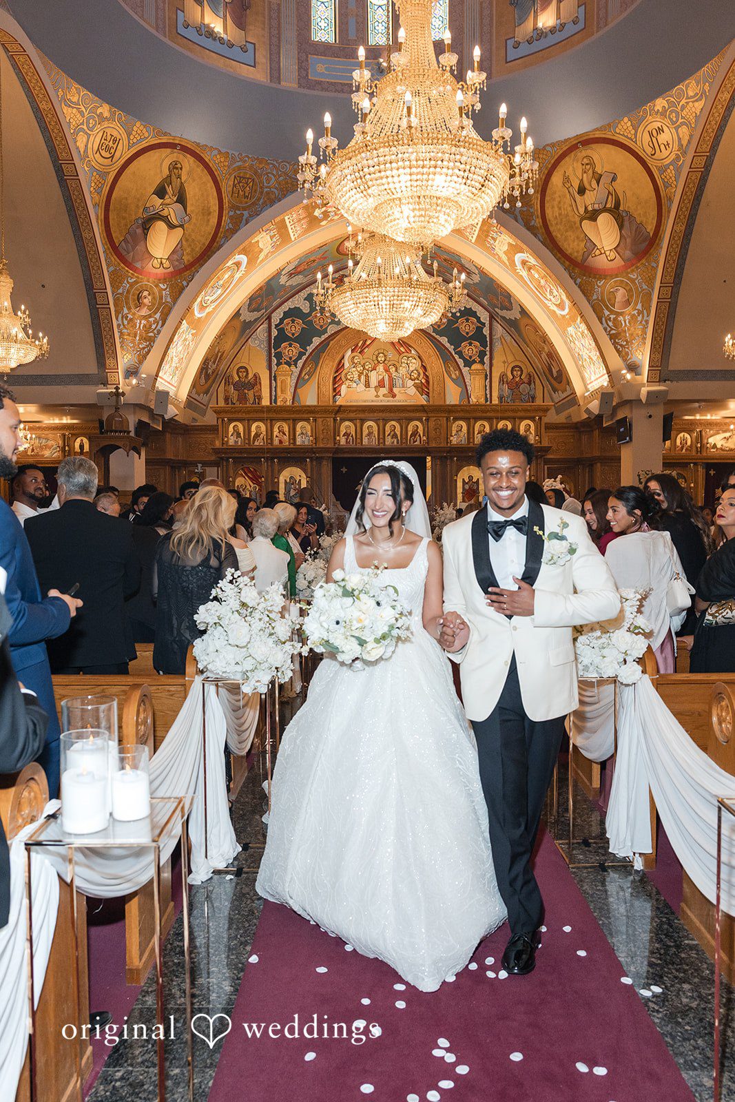 A bride and groom walking down a church aisle together smiling.