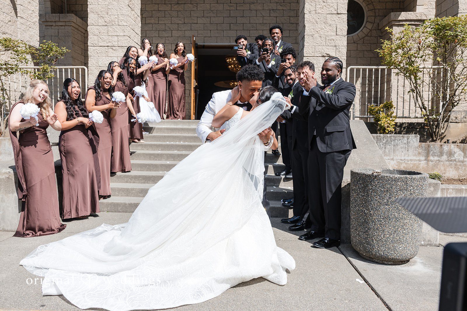 A groom lifting his bride's veil outside a building.
