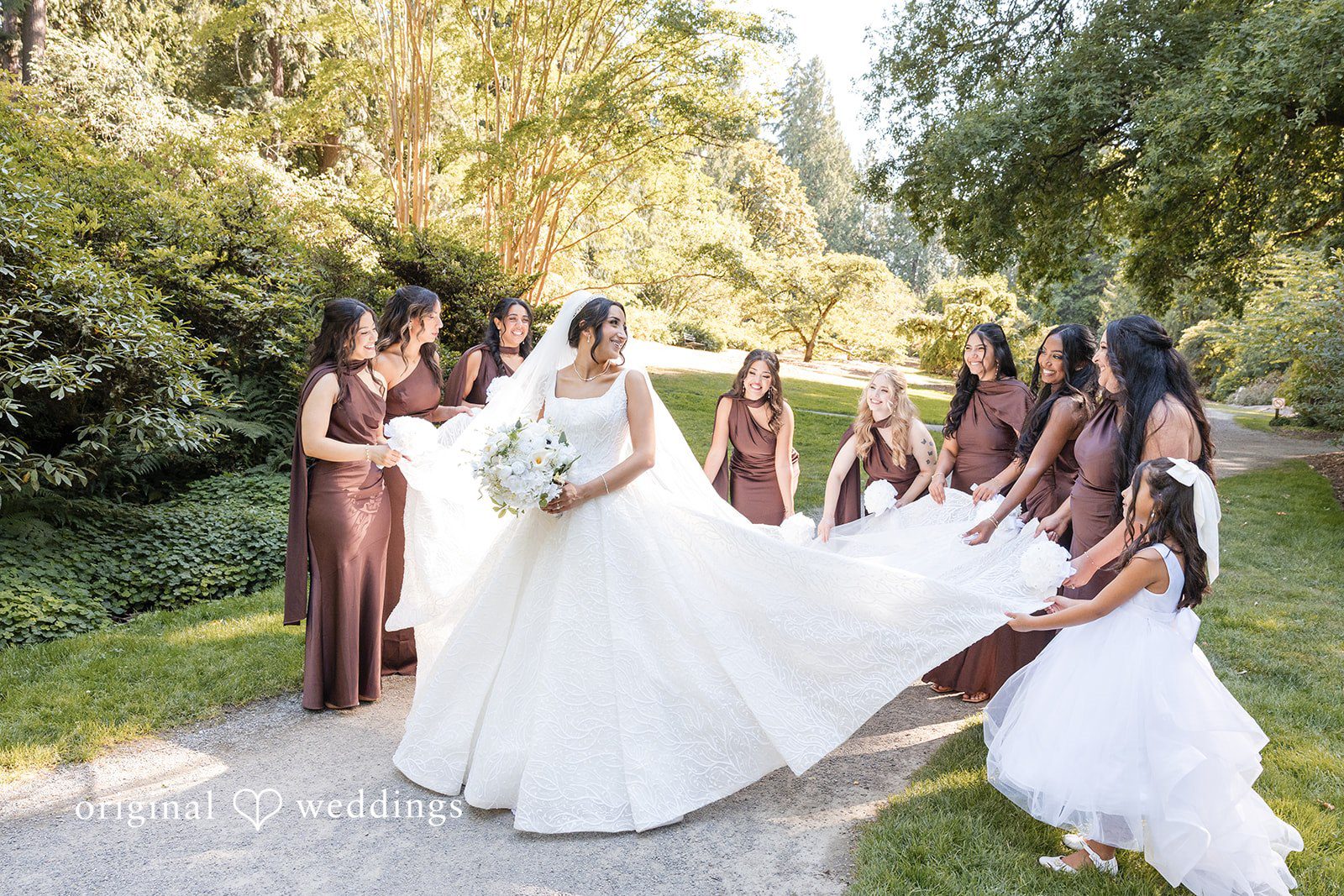 A bride surrounded by several bridesmaids adjusting her long veil.