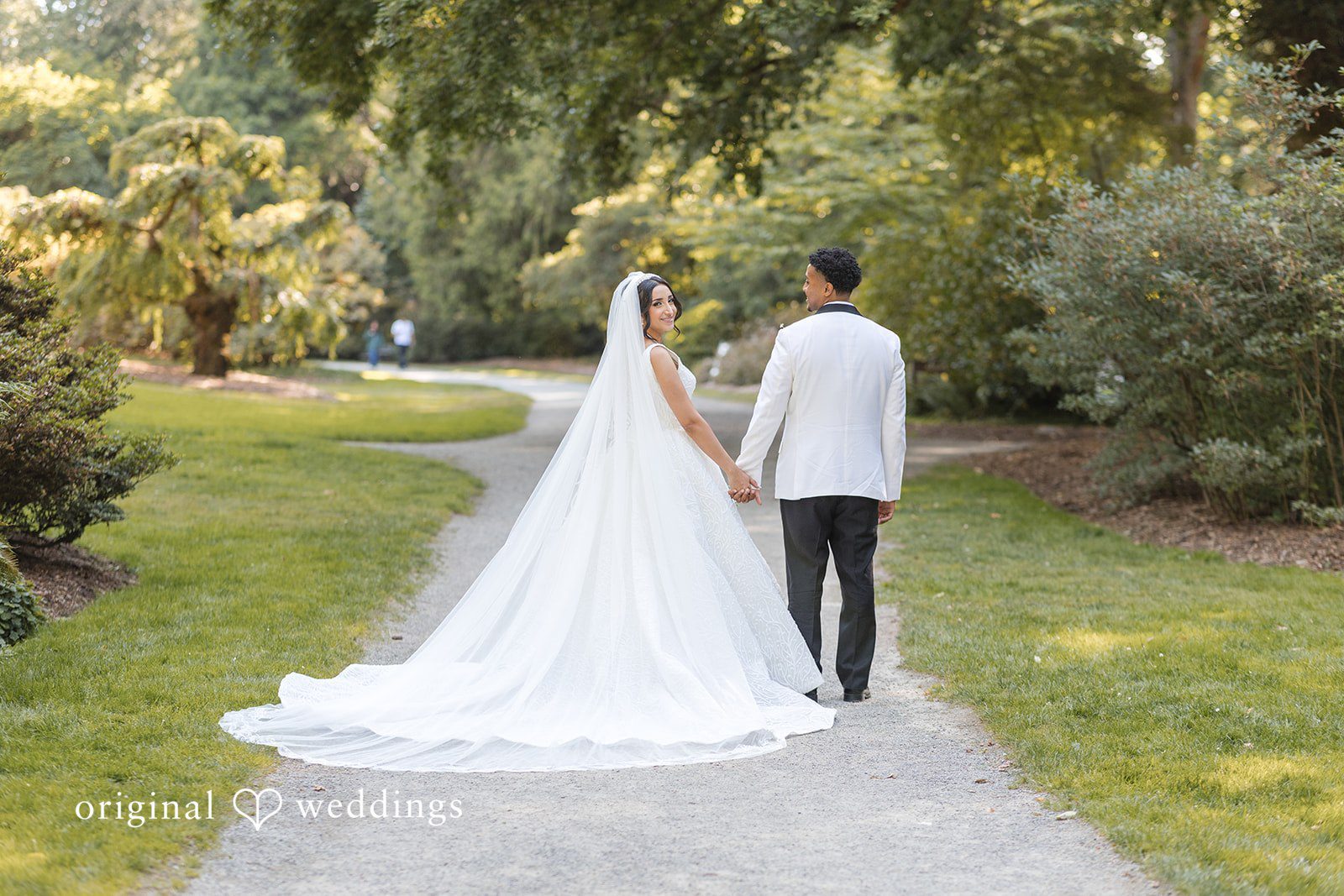A bride and groom standing on a path, viewed from behind.