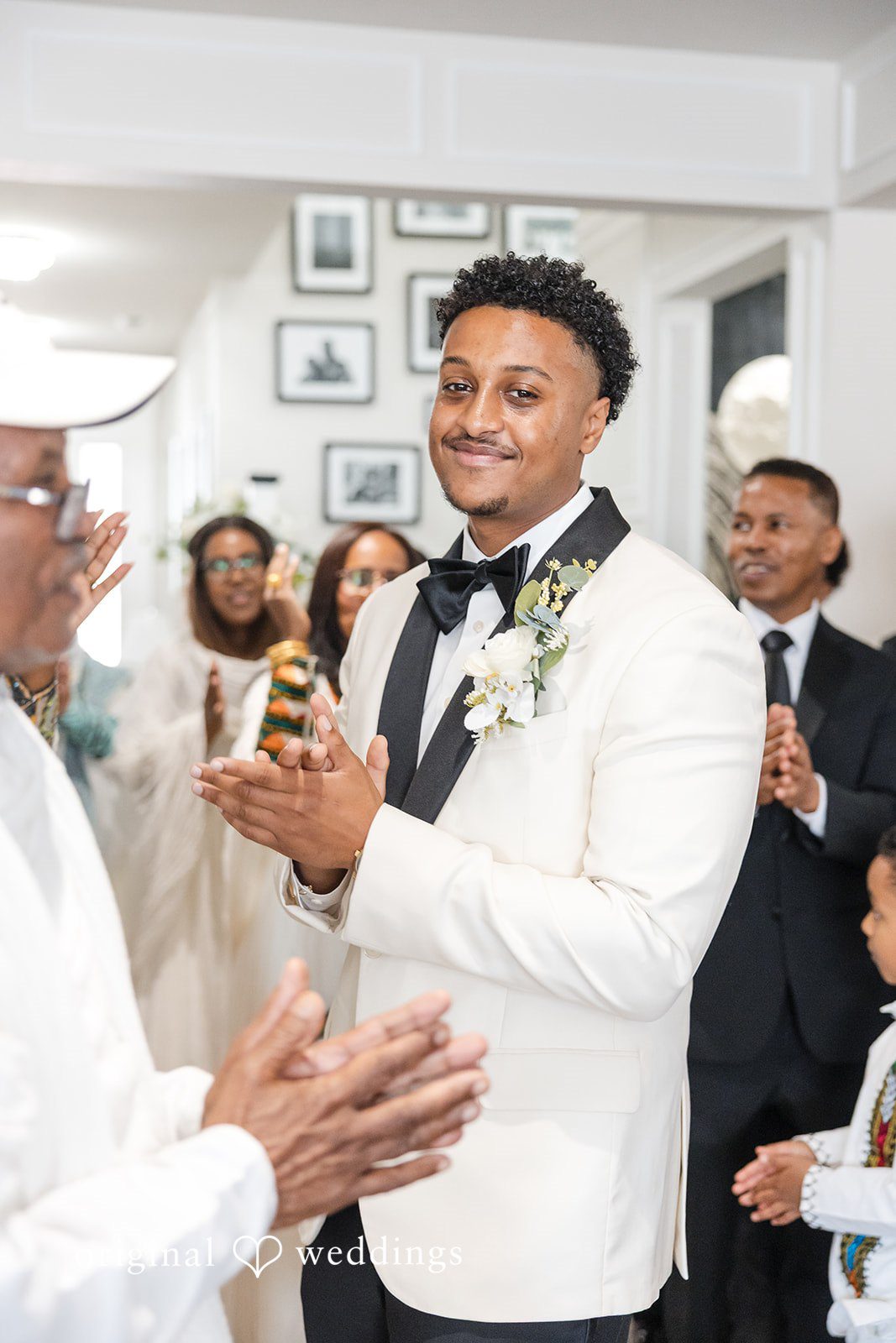 A groom smiling while surrounded by wedding guests clapping.