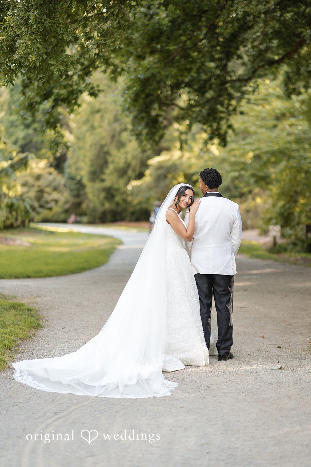 A bride and groom embracing on a tree-lined path.