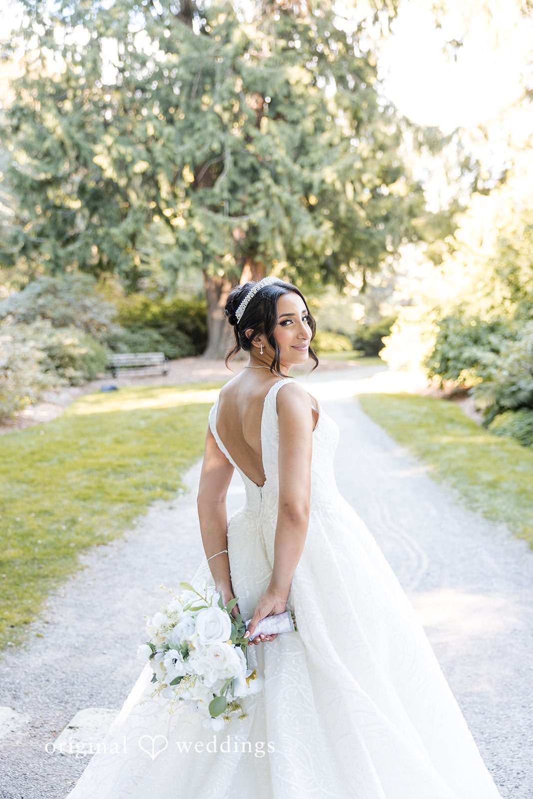 A bride posing on a pathway, showing the long train of her white dress.