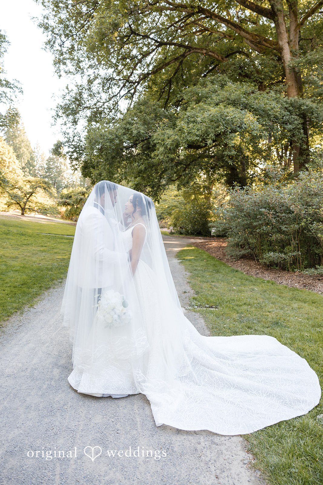 A bride kneeling on the grass with her long veil spread out.