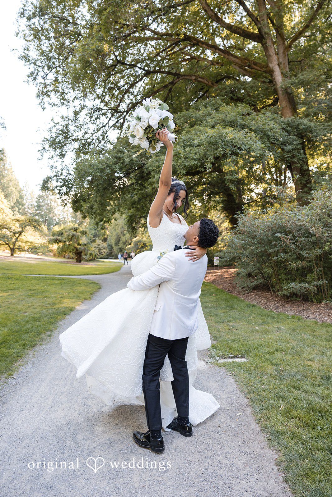 A groom lifting and spinning his bride on a pathway.