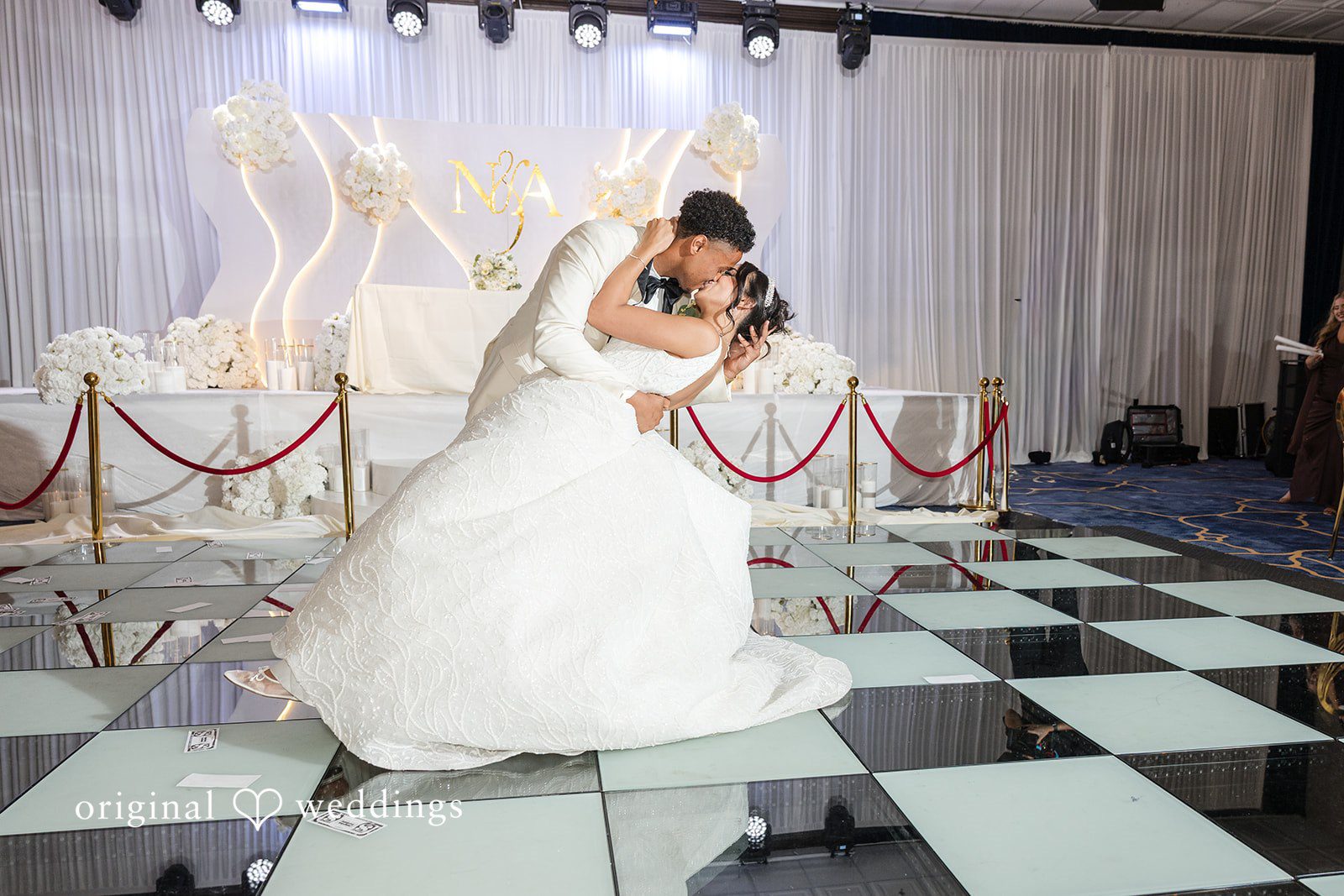 A groom dipping and kissing his bride on a checkered dance floor.