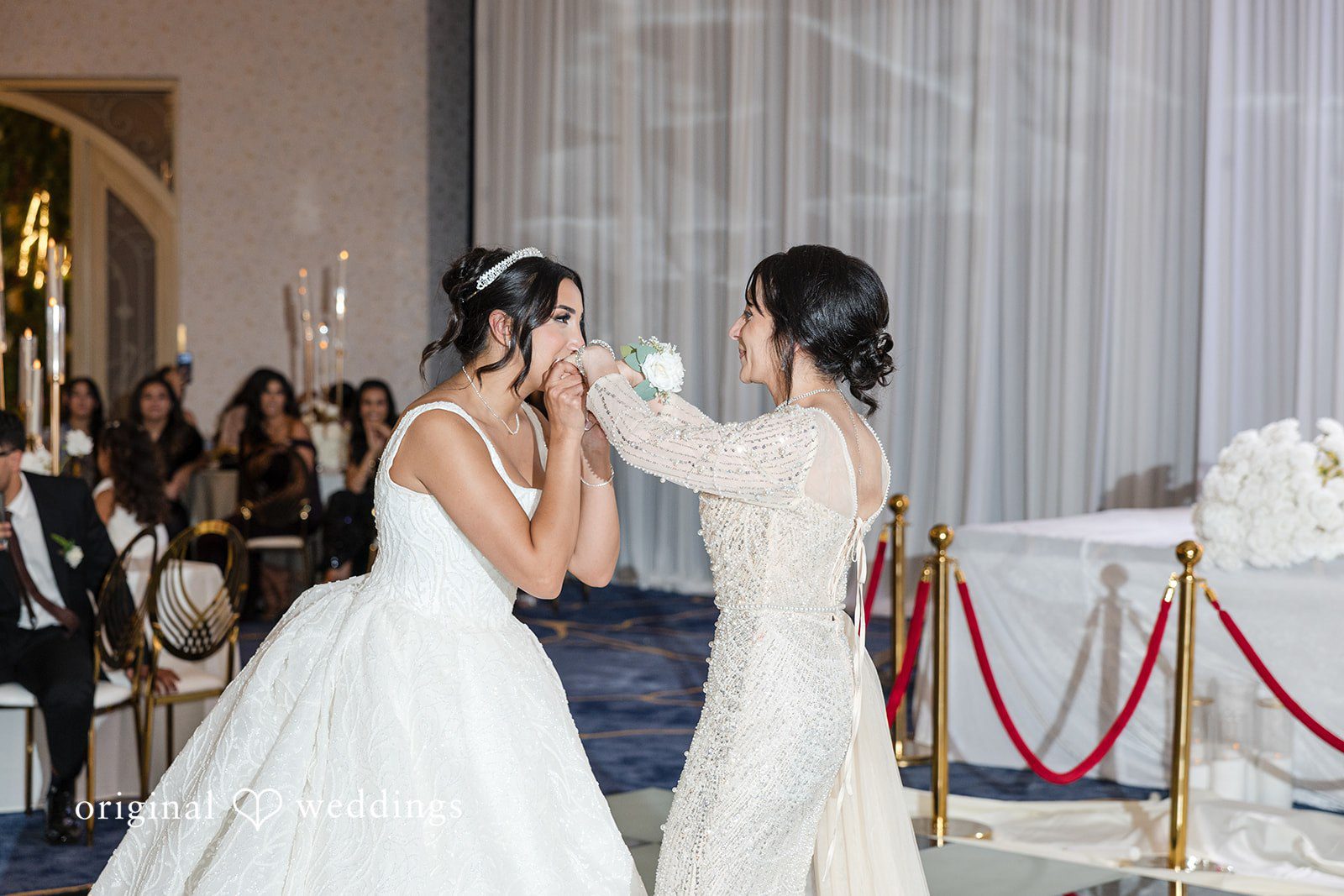 A bride wiping away tears with a tissue while another woman comforts her.