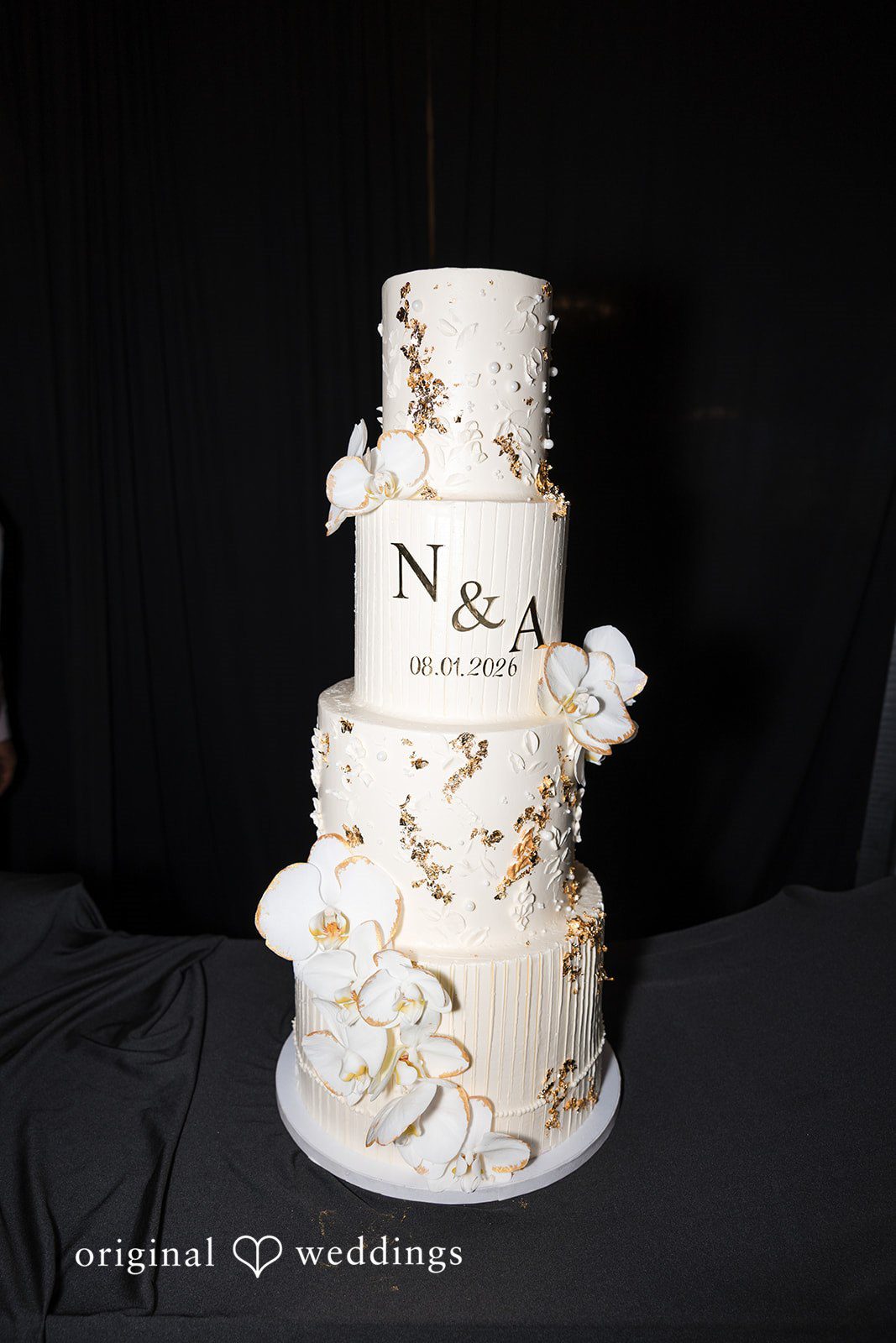 A three-tiered white wedding cake decorated with initials and flowers.