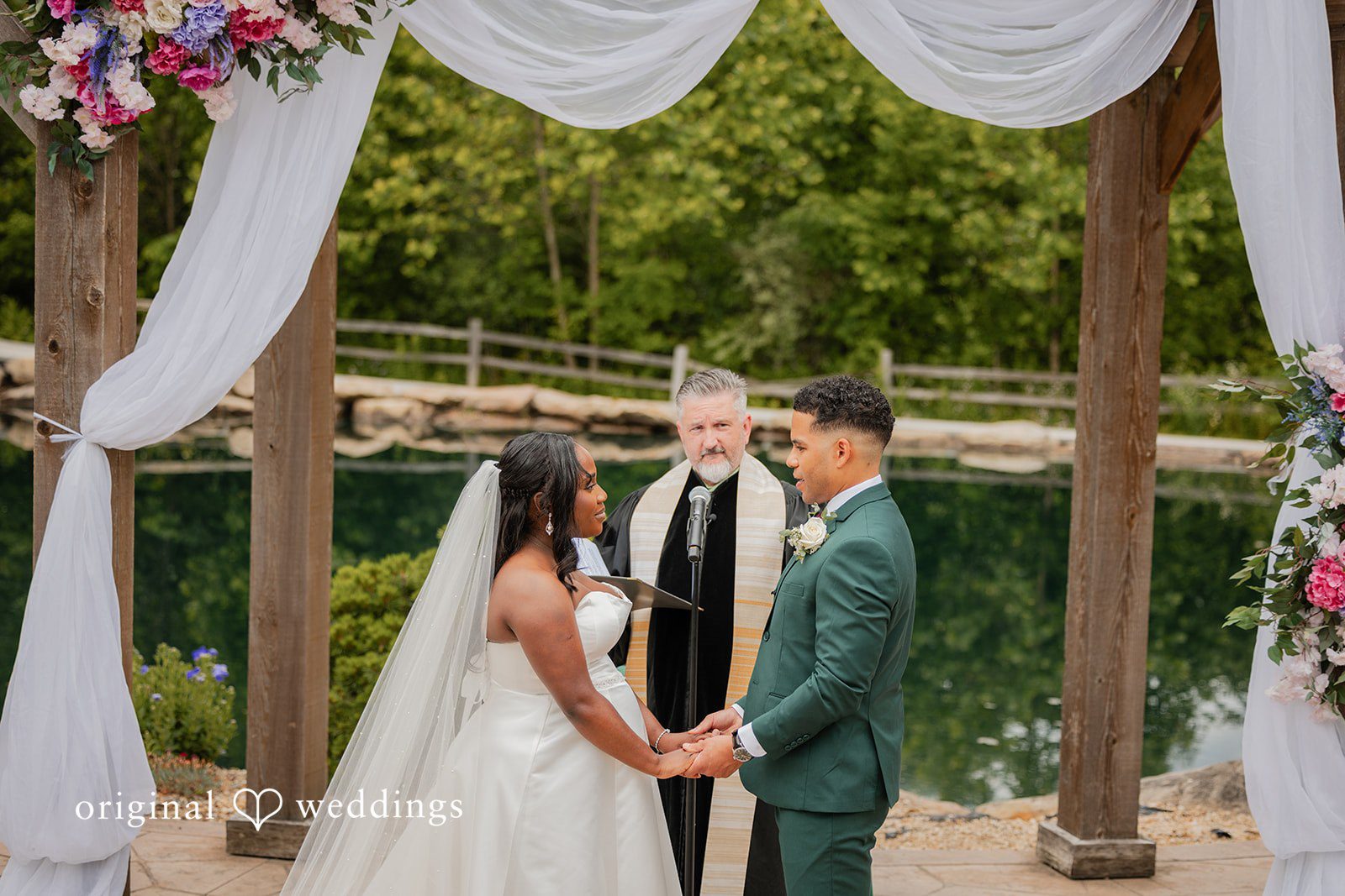 Christopher + Maxine Bride and groom holding hands facing each other under a draped fabric wedding archway.