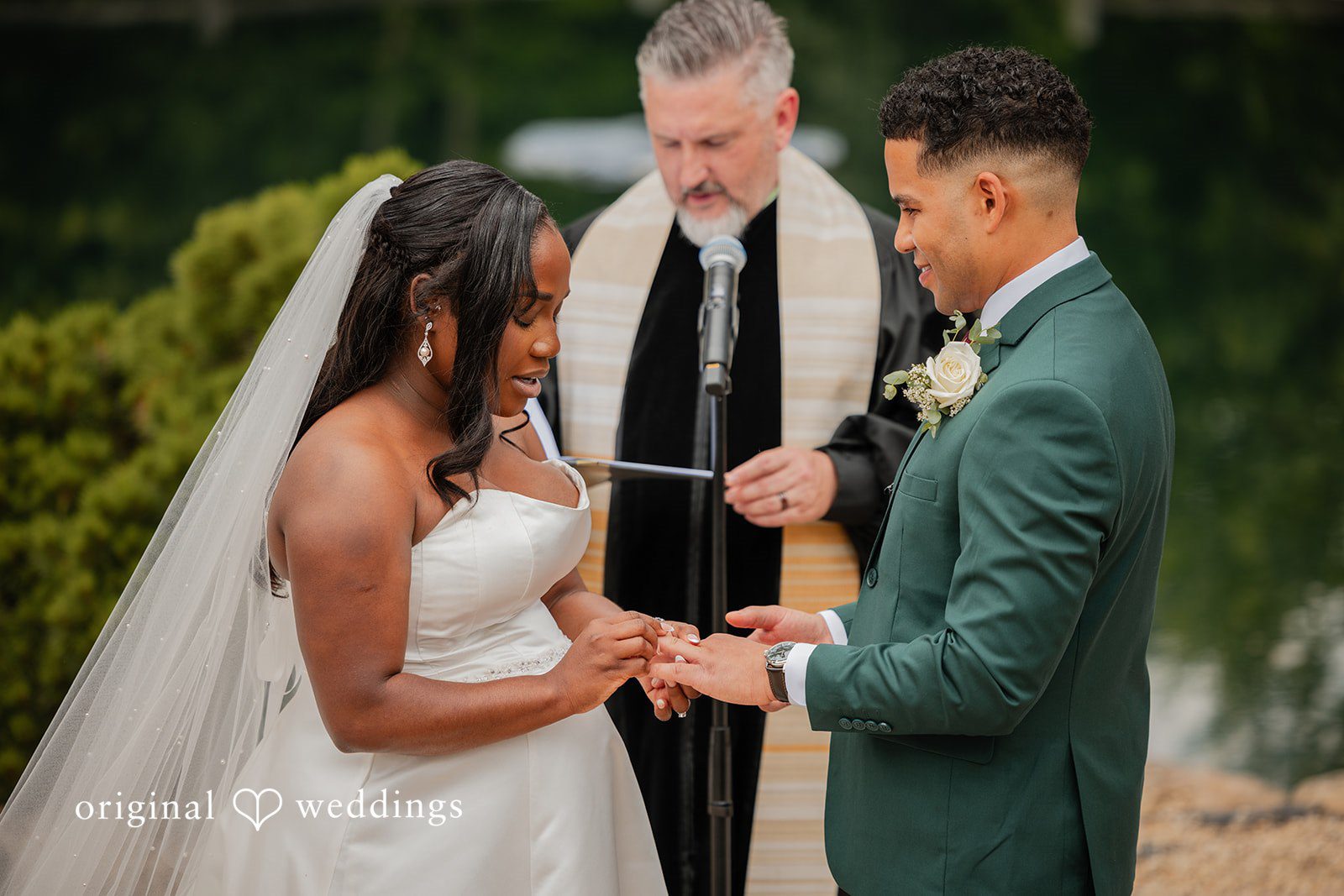 Christopher + Maxine Groom placing a ring on the bride's finger during a wedding ceremony with an officiant present.