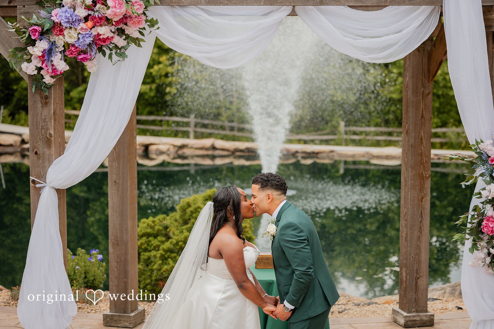 Christopher + Maxine Bride and groom sharing a kiss beneath a white draped wedding archway.