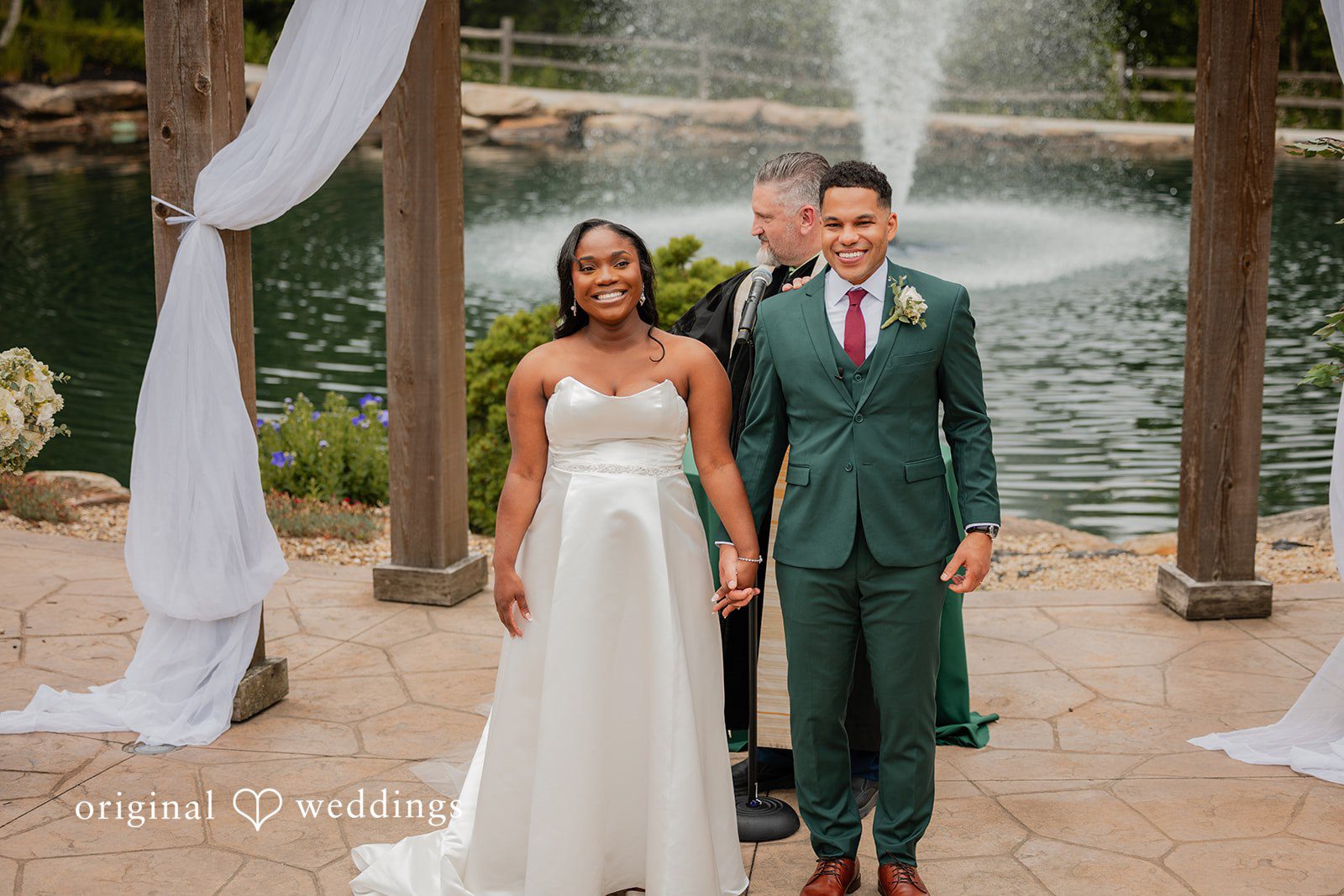 Christopher + Maxine Bride and groom holding hands while posing together in front of a stone architectural background.