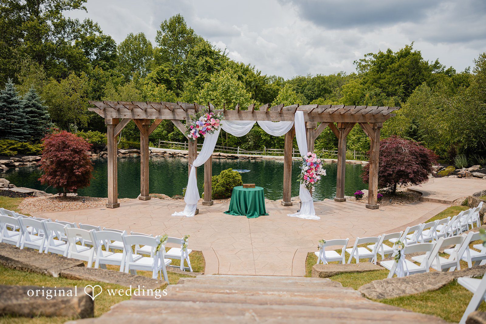 Christopher + Maxine Wedding ceremony altar decorated with white fabric curtains and floral arrangements overlooking rows of clear chairs.