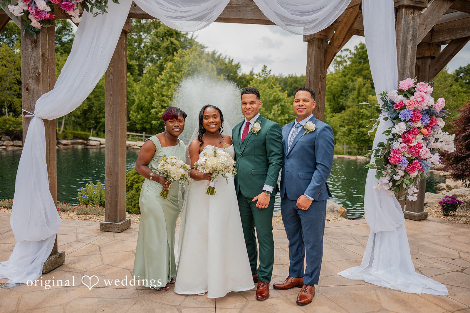 Christopher + Maxine Four members of a wedding party posing together in formal attire under a draped archway.