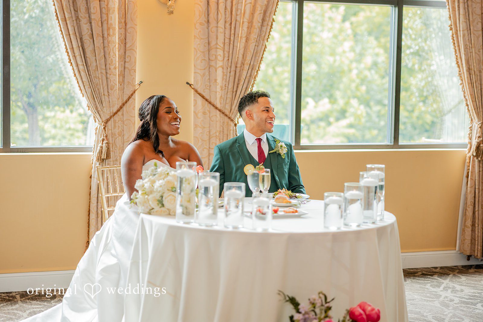 Christopher + Maxine Newlyweds seated at a decorated sweetheart table inside a reception venue.