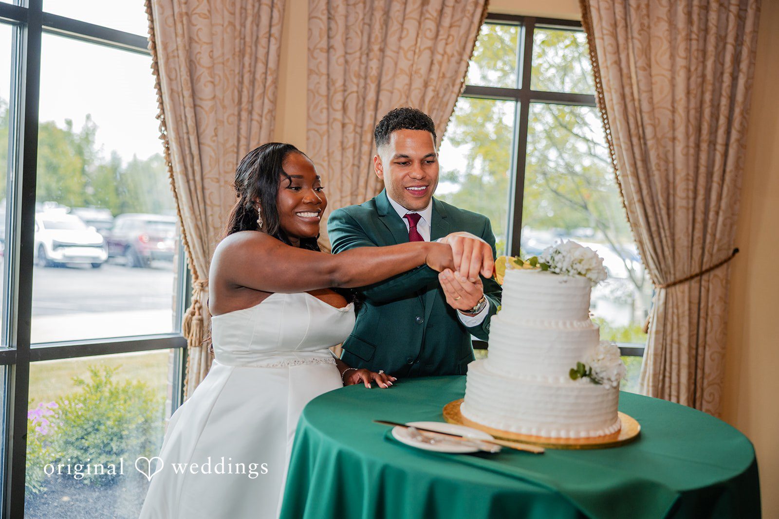 Christopher + Maxine Bride and groom cutting a tiered wedding cake placed on a green tablecloth.