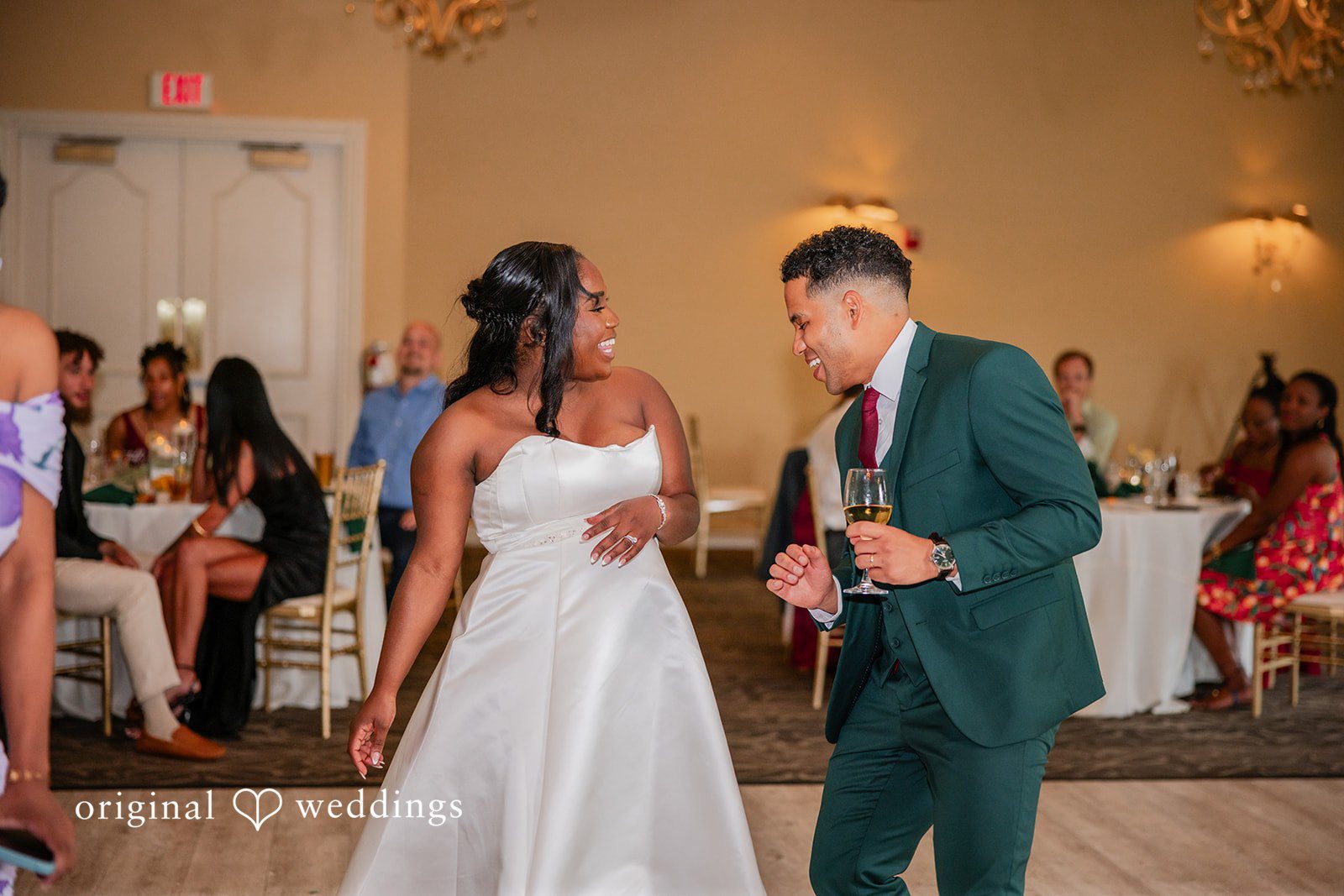 Christopher + Maxine Groom speaking into a microphone while standing next to his dancing bride.