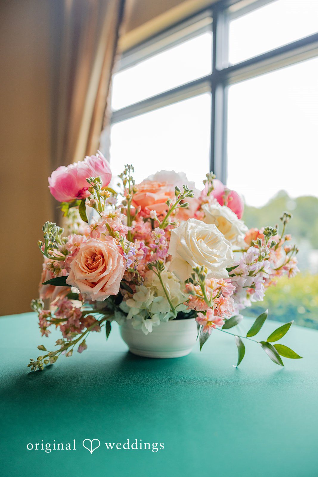 Christopher + Maxine Close-up of a floral centerpiece with pink and white flowers arranged on a green tablecloth.