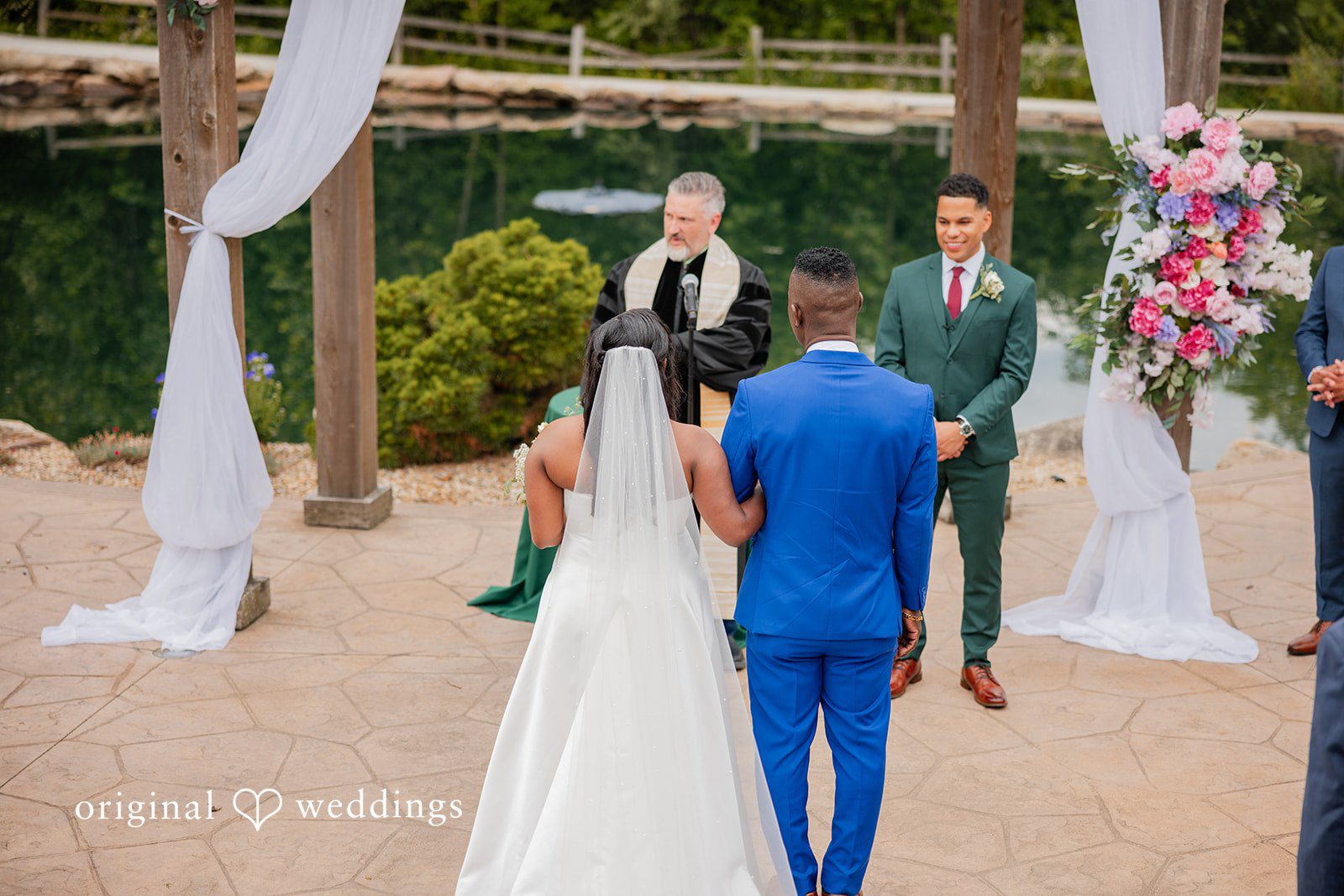 Christopher + Maxine Wedding ceremony in progress under a decorated archway with guests looking on from behind.