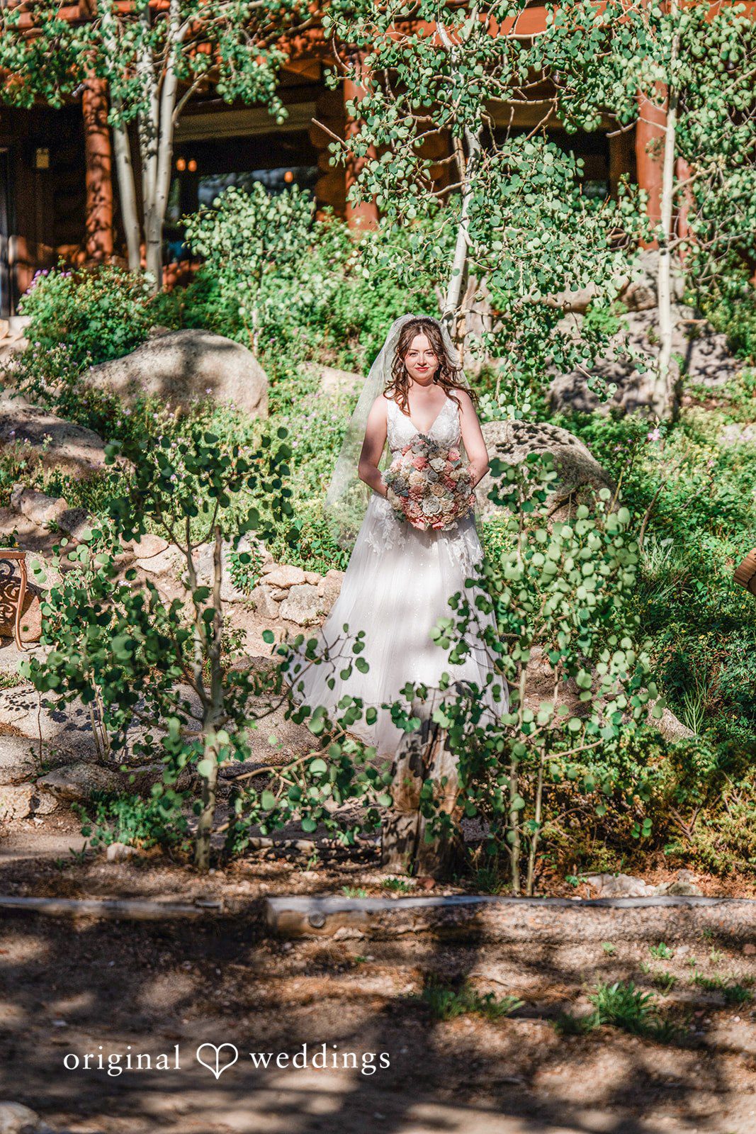 Madelyn + Erin A bride sitting alone on a swing surrounded by tall pine trees.