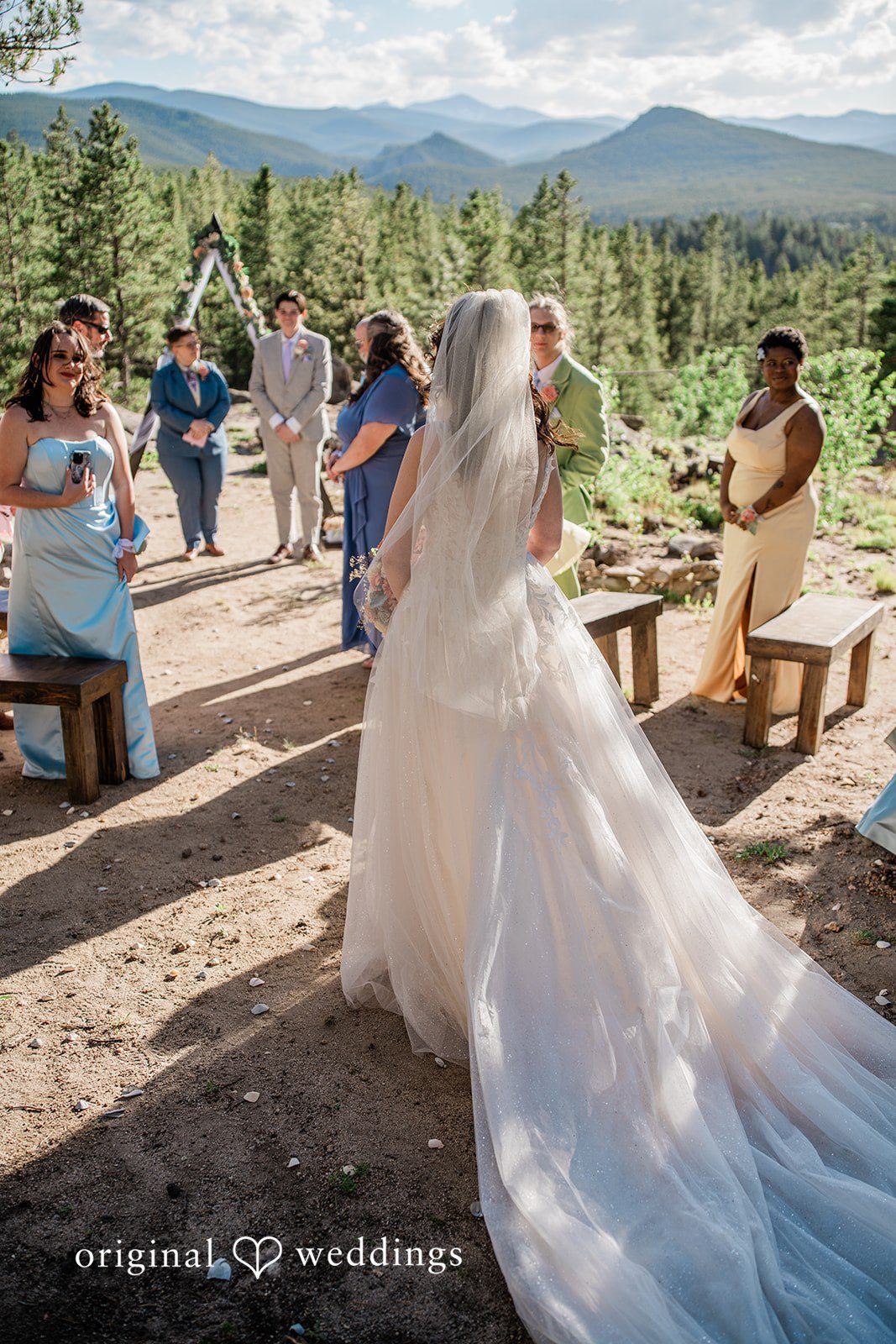 Madelyn + Erin A bride walking down a path with her long white dress train trailing behind.