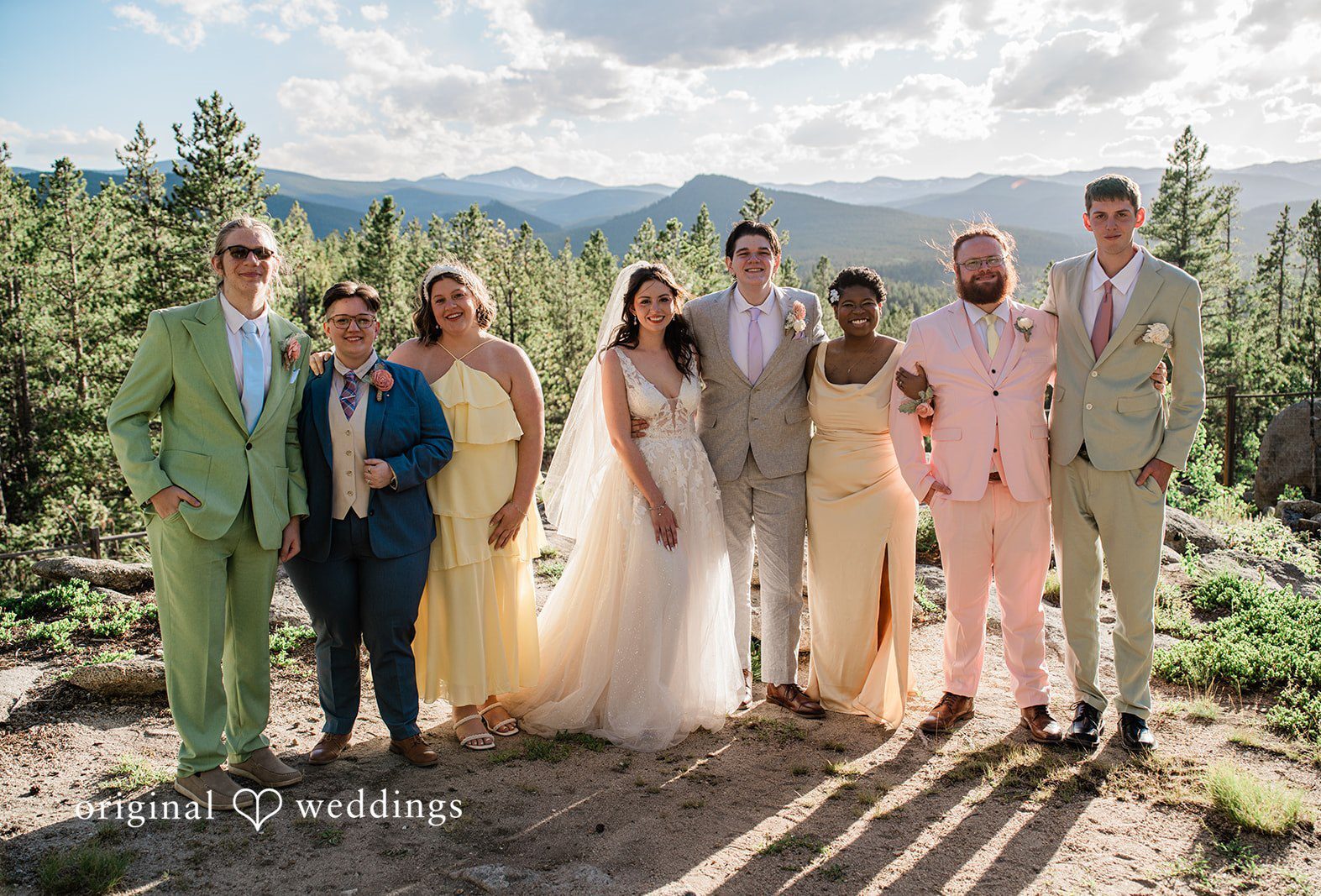 A wedding party standing together for a group photo in front of a mountain landscape at Blue Sky Mountain Ranch by Denver Wedding Photographers from Original Weddings.