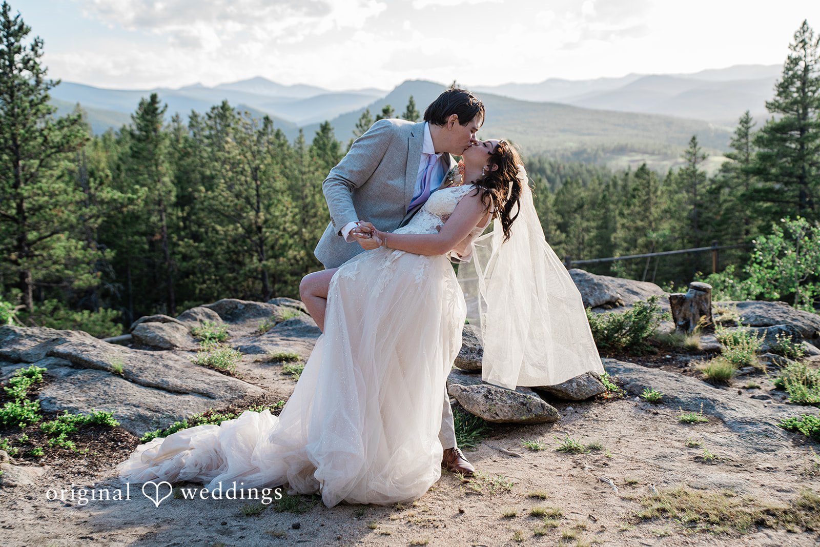 Madelyn + Erin A bride and groom sharing a hug among mountain greenery.
