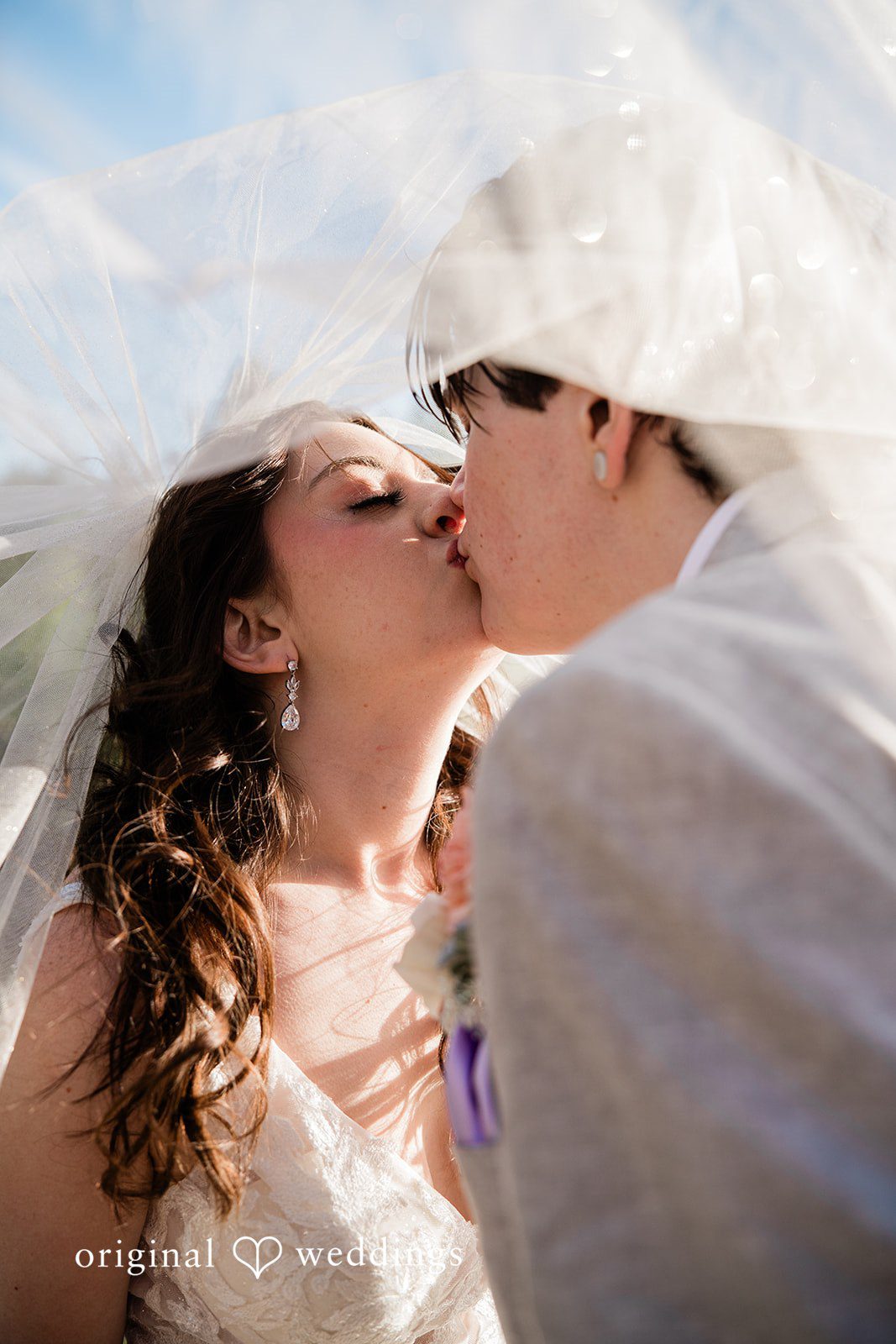 Madelyn + Erin A close-up of a bride and groom sharing a kiss under a veil.