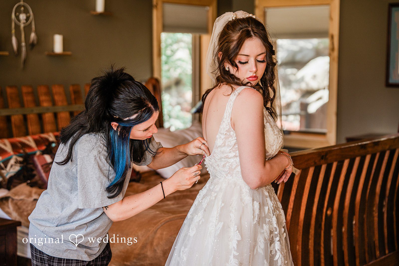 Madelyn + Erin A woman helping a bride adjust the back of her white wedding dress.