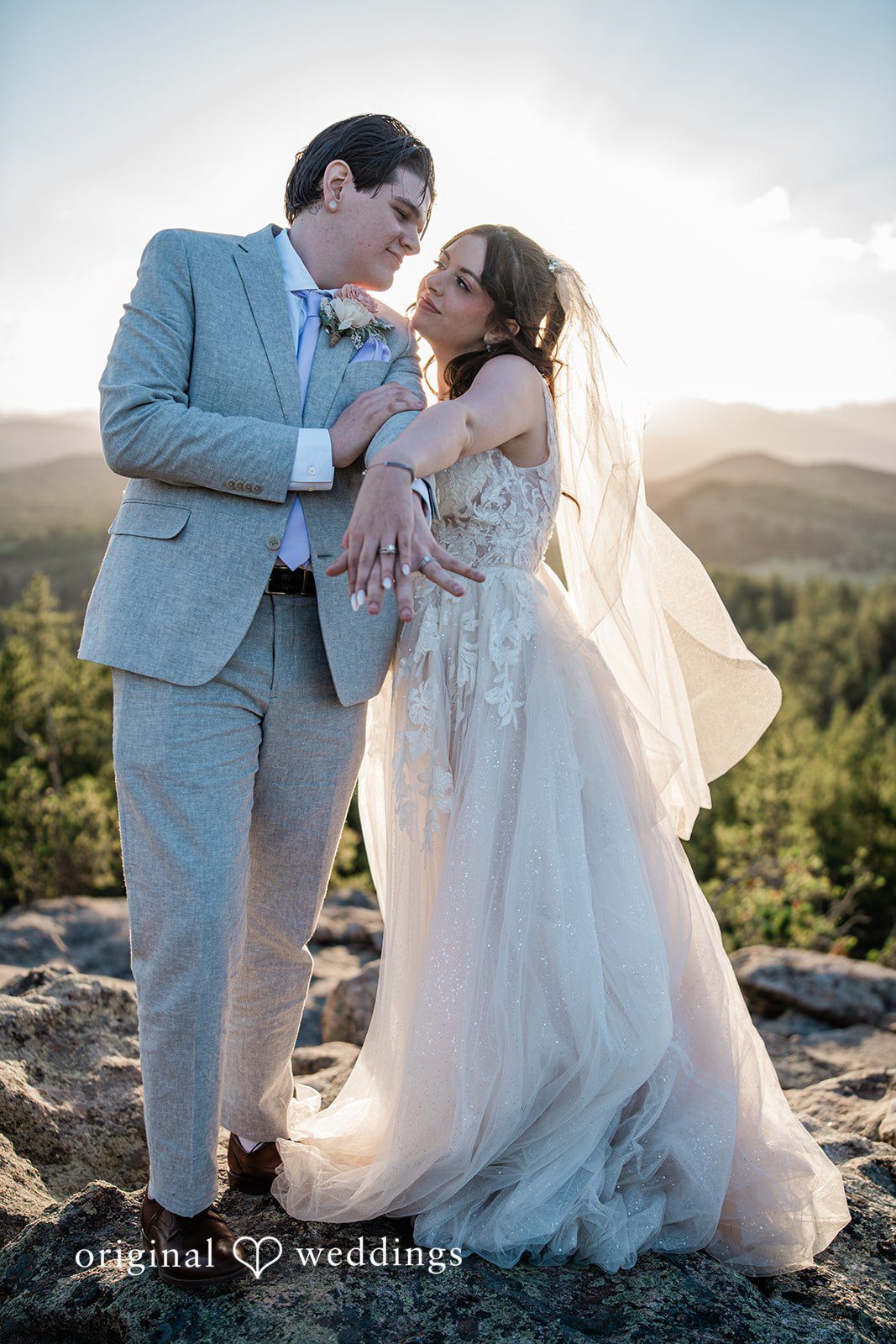 Madelyn + Erin A groom smiling down at his bride as they embrace on a rocky overlook.