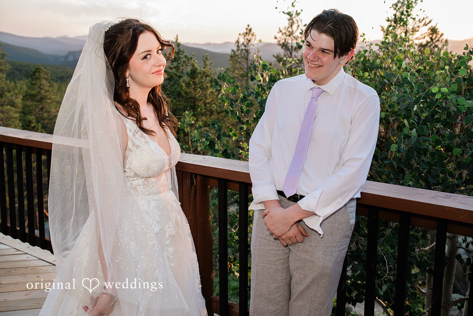 Madelyn + Erin A bride and groom standing together on a wooden balcony overlooking greenery.