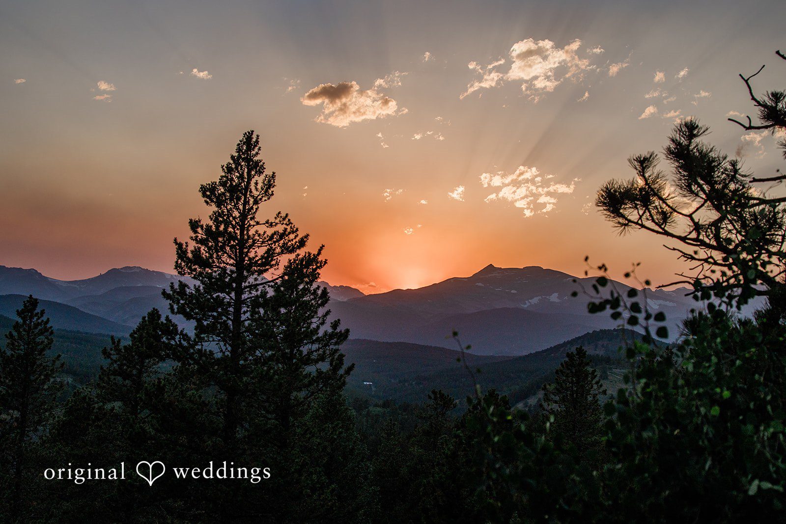Madelyn + Erin A scenic sunset view over a vast, forested mountain range.