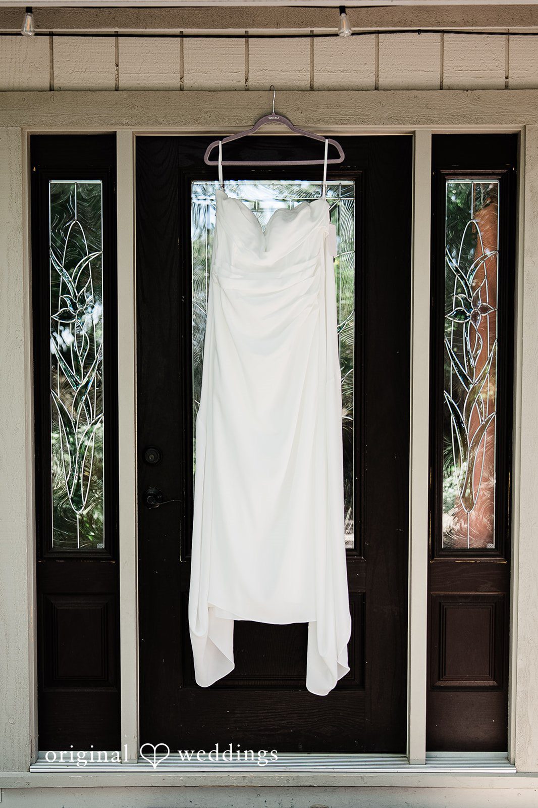 Lindsay + Ryan A white wedding dress hanging elegantly in a dark wooden doorway framed by glass panels.