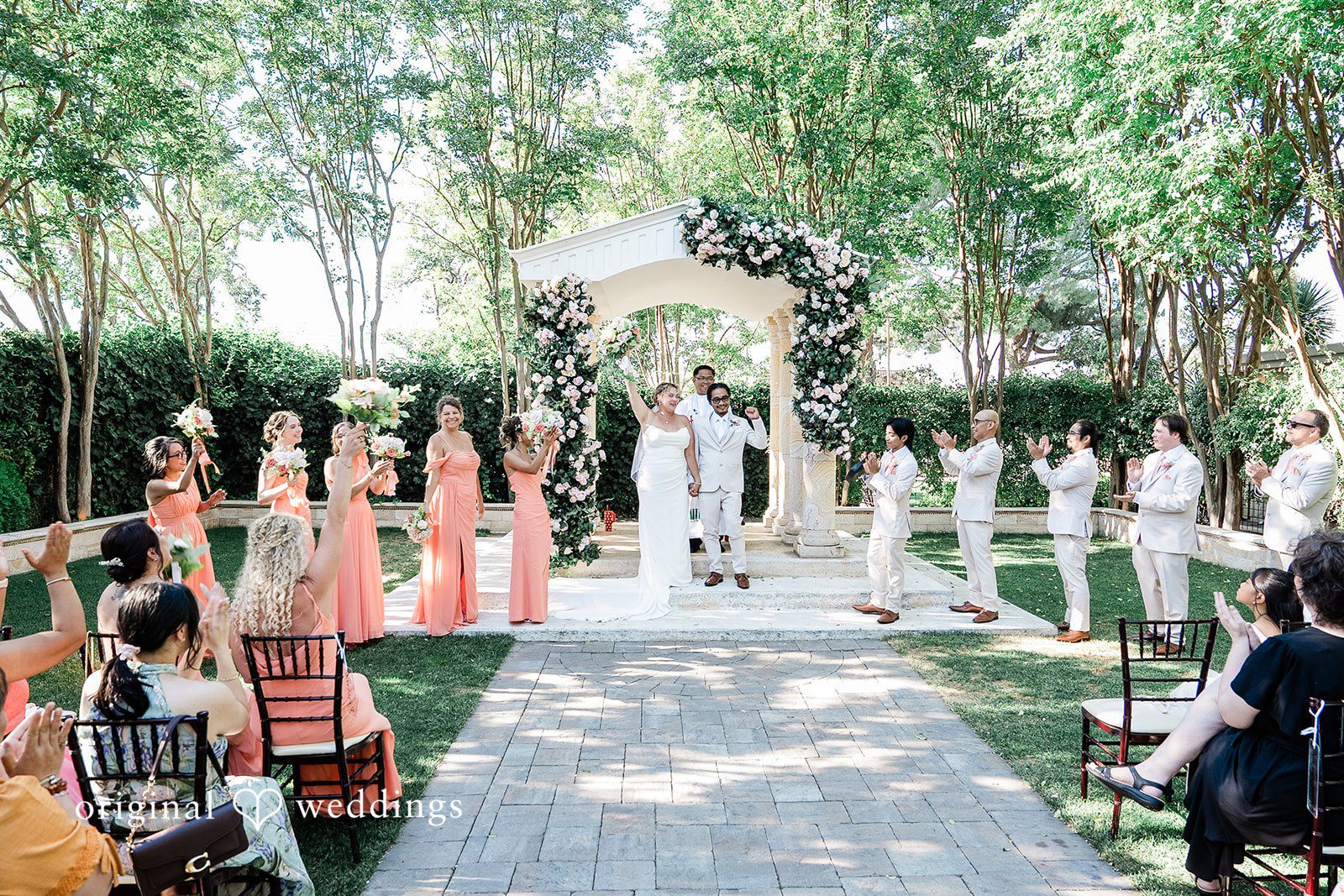 Lindsay + Ryan A wide view of a wedding ceremony aisle lined with white chairs and greenery.