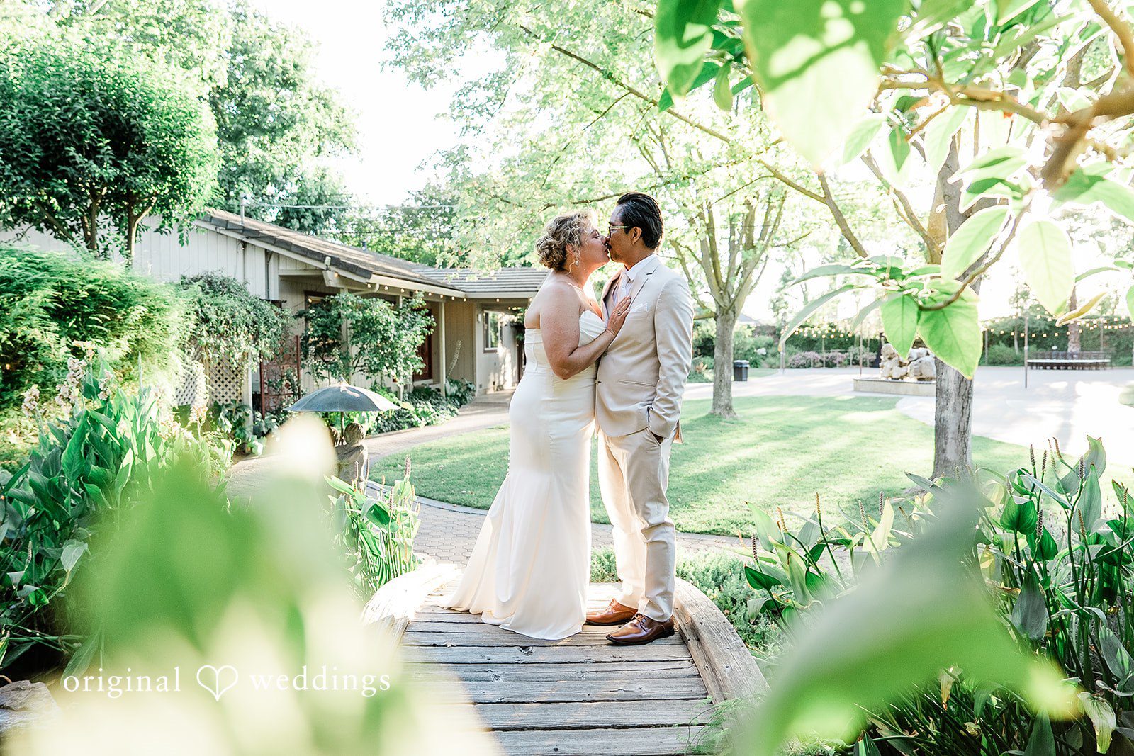 Lindsay + Ryan A bride and groom sharing a quiet kiss on a wooden bridge surrounded by foliage.