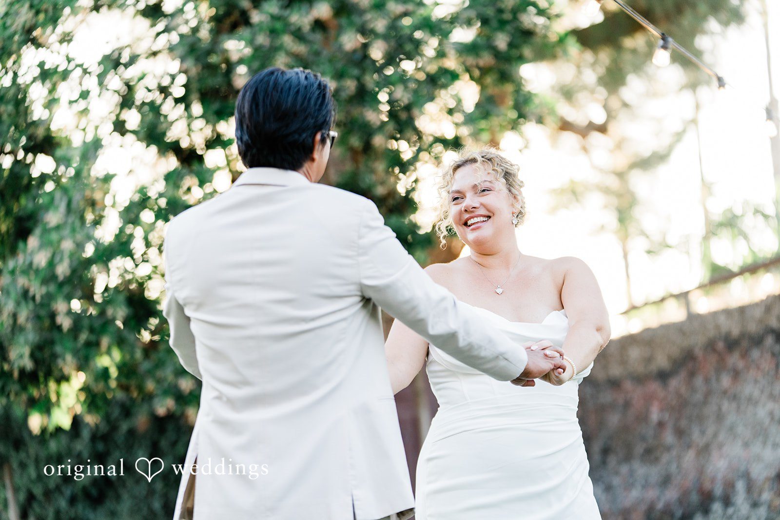 Lindsay + Ryan A groom in a light suit holding hands with his smiling bride in a sunlit setting.