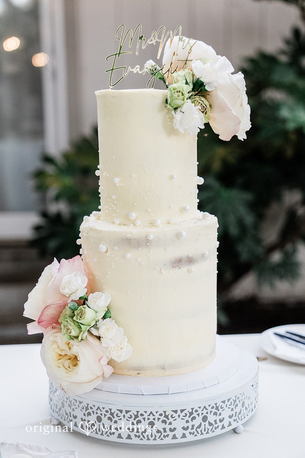 Lindsay + Ryan A three-tiered white wedding cake decorated with soft pink and white floral accents.