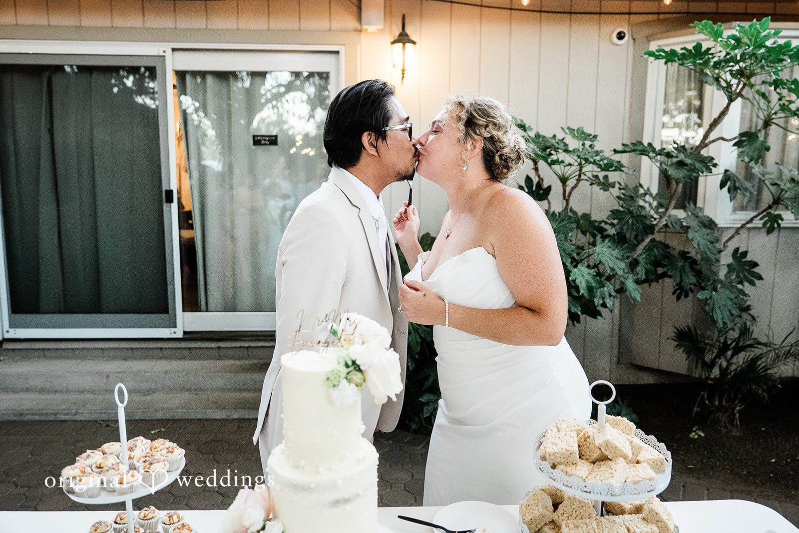 Lindsay + Ryan A bride and groom sharing a sweet kiss next to a dessert table.