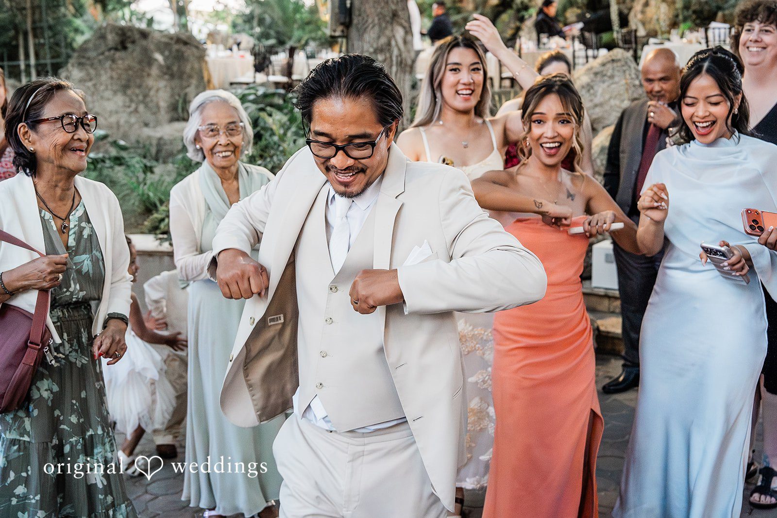Lindsay + Ryan A groom in a light suit dancing energetically surrounded by cheering wedding guests.