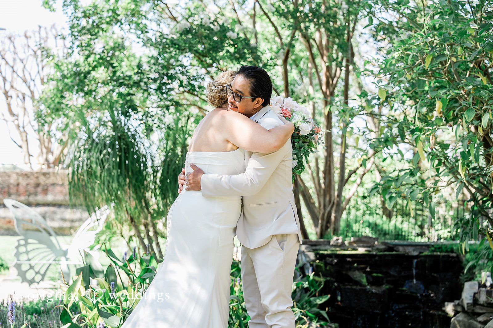 Lindsay + Ryan A bride and groom hugging tightly near lush green trees during their wedding day.