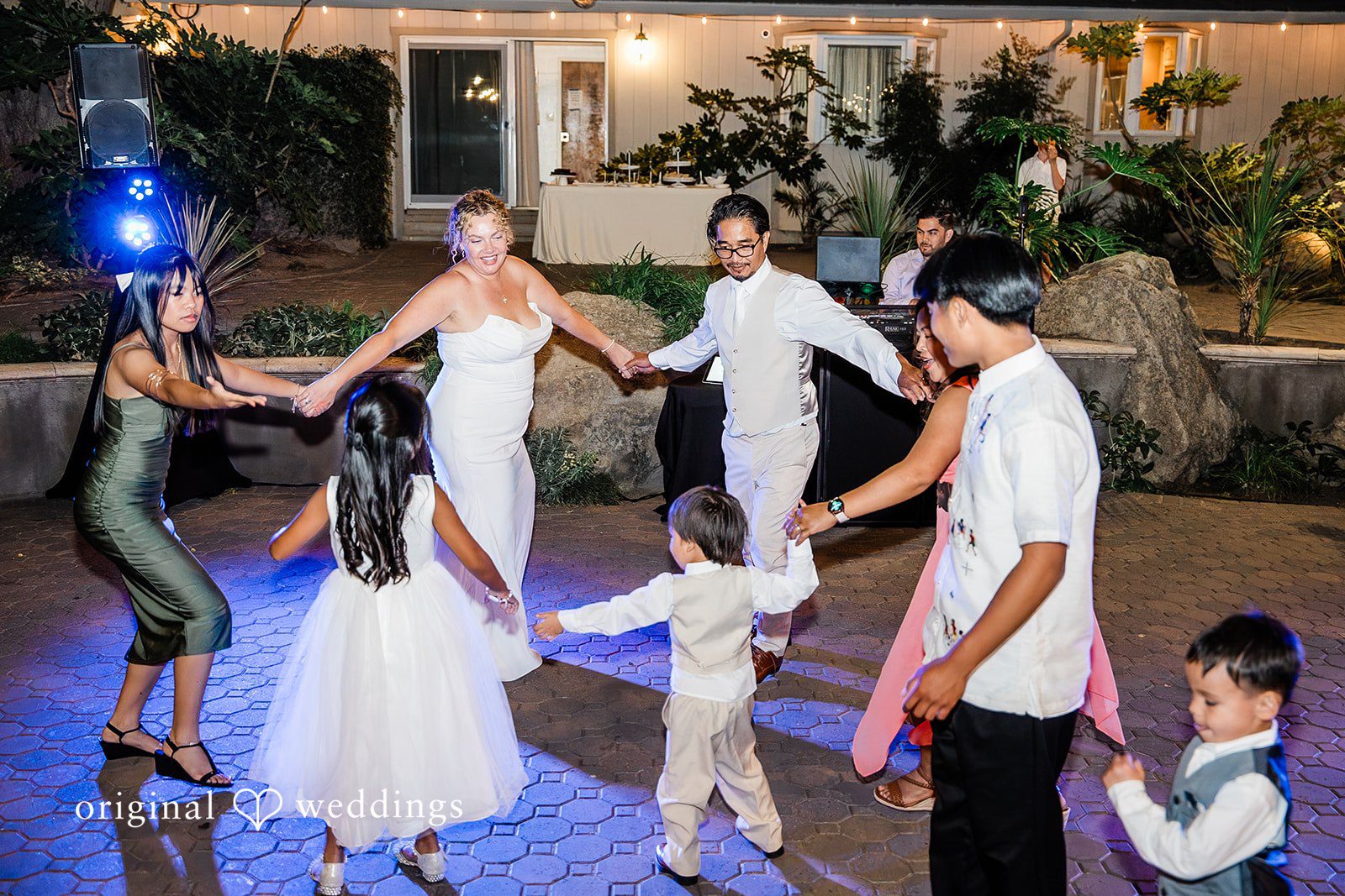 Lindsay + Ryan A bride and groom dancing with a child on a lit reception dance floor.