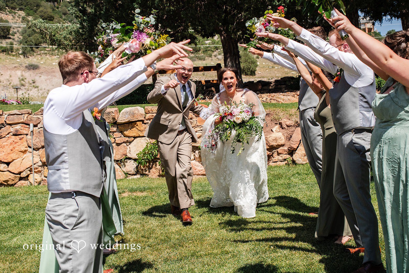 Mckenna + Ryan A bride and groom walking down a path as guests raise their arms in celebration.